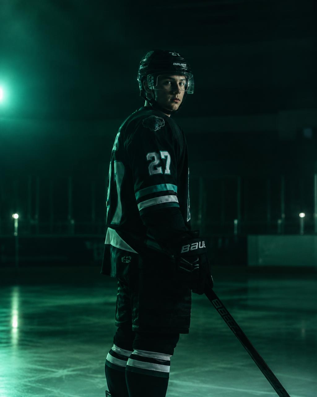 A young hockey player in full gear on a dark rink under cool green light